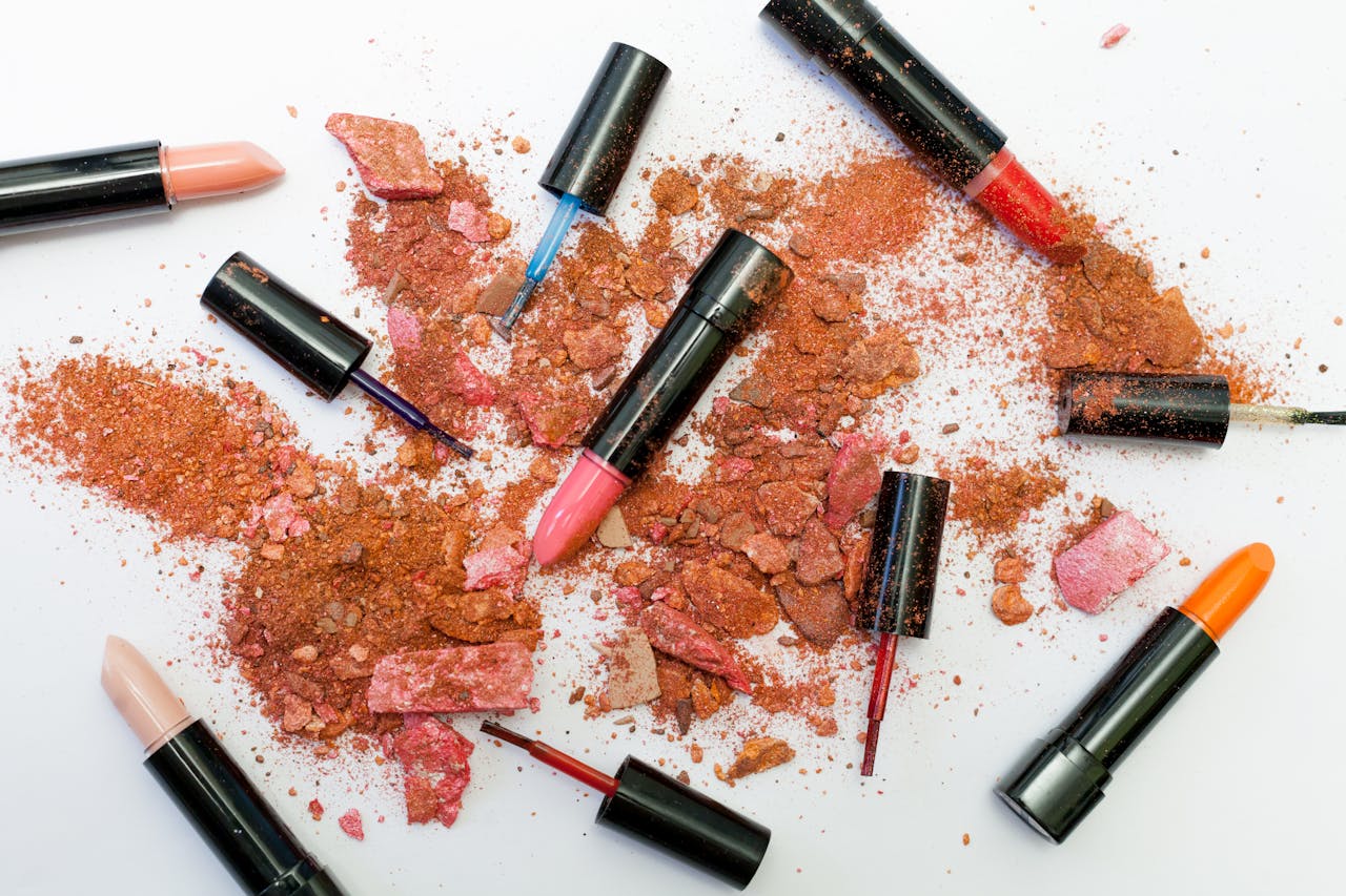 gallery-1 Colorful scattered makeup products including lipsticks and crushed powders on a white background.