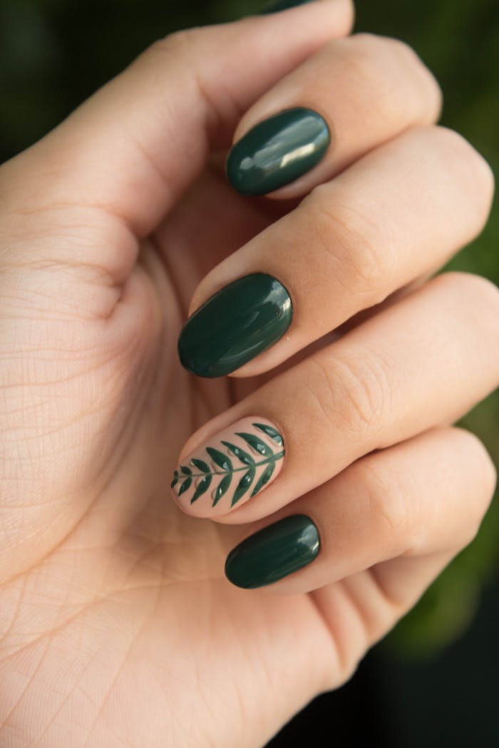 gallery-4 Close-up of a stylish green manicure with a leaf design, showcasing glossy fingernails and natural skin tone.